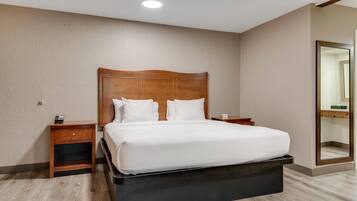 A hotel room with a large bed, wooden headboard, two bedside tables, and a mirror on the wall.
