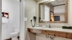 A bathroom with a toilet, a sink with a mirror, and a hairdryer on the wall. - Suburban Studios near Mesa Verde (Cortez)