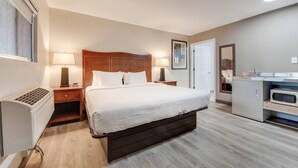 A hotel room with a bed, bedside lamps, a small table, a heater, a wardrobe, and a kitchenette. - Suburban Studios near Mesa Verde (Cortez)