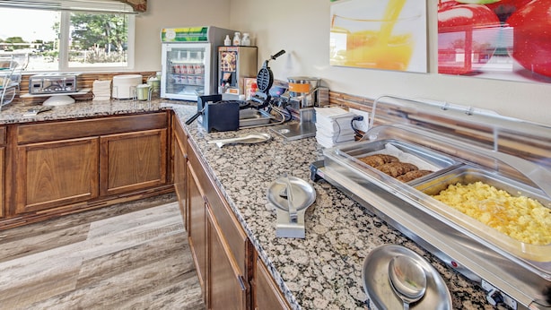 A breakfast area with a granite countertop, a waffle maker, a coffee machine, and a refrigerator stocked with beverages. - Suburban Studios near Mesa Verde (Cortez)