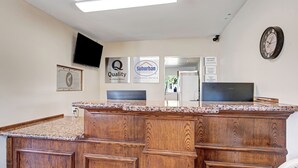 A reception area with a wooden counter, a flat-screen TV, and signs for 'Quality by Choice Hotels' and 'Suburban'. - Suburban Studios near Mesa Verde (Cortez)