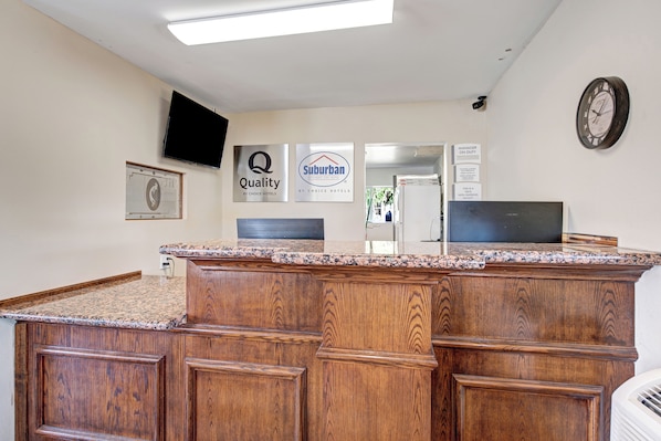Un espace d’accueil avec un comptoir en bois, un téléviseur à écran plat et des panneaux indiquant « Qualité garantie par Choice Hotels » et « Suburban ».