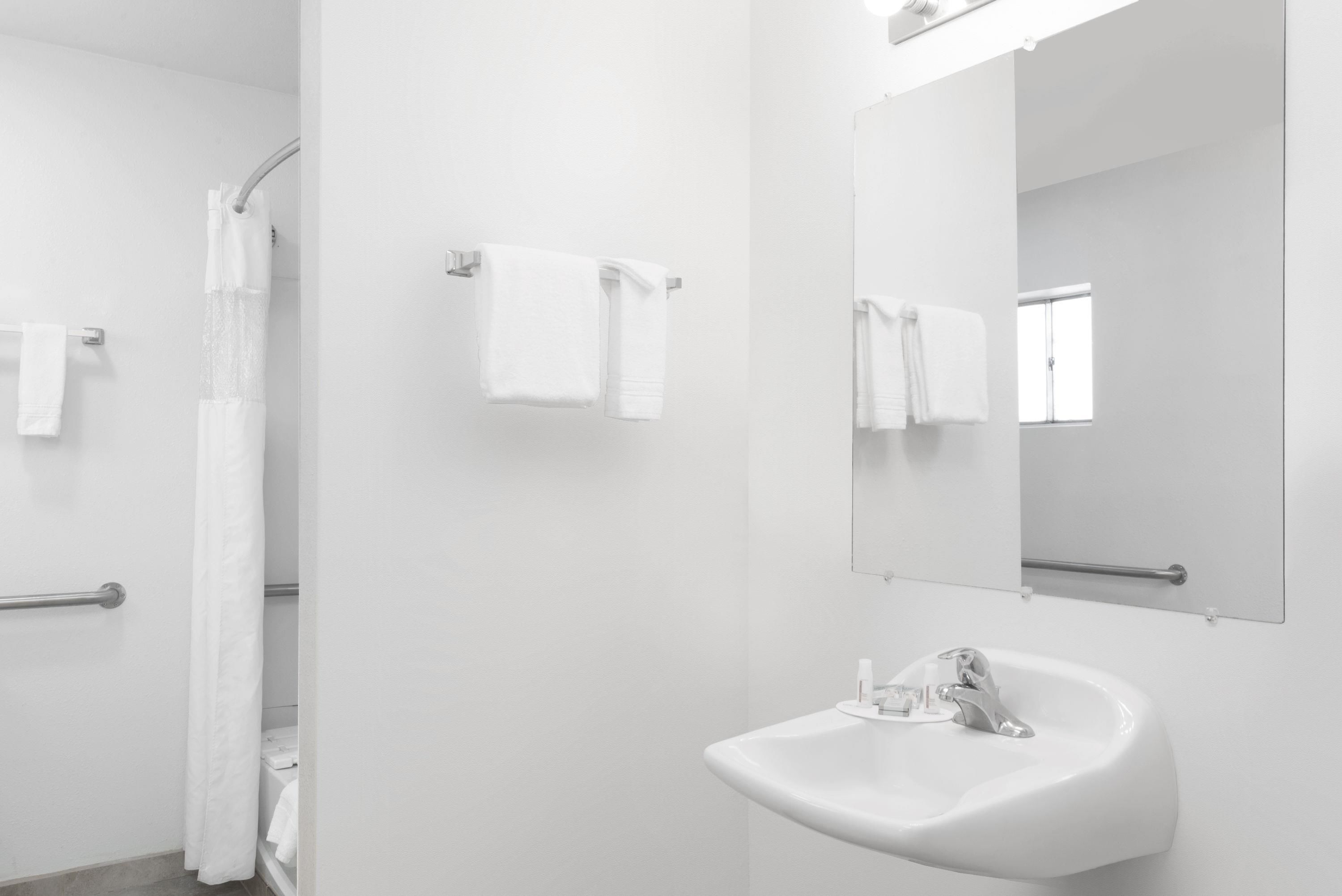 Un baño moderno con un lavamanos blanco, un espejo y dos toallas colgadas en toalleros.
