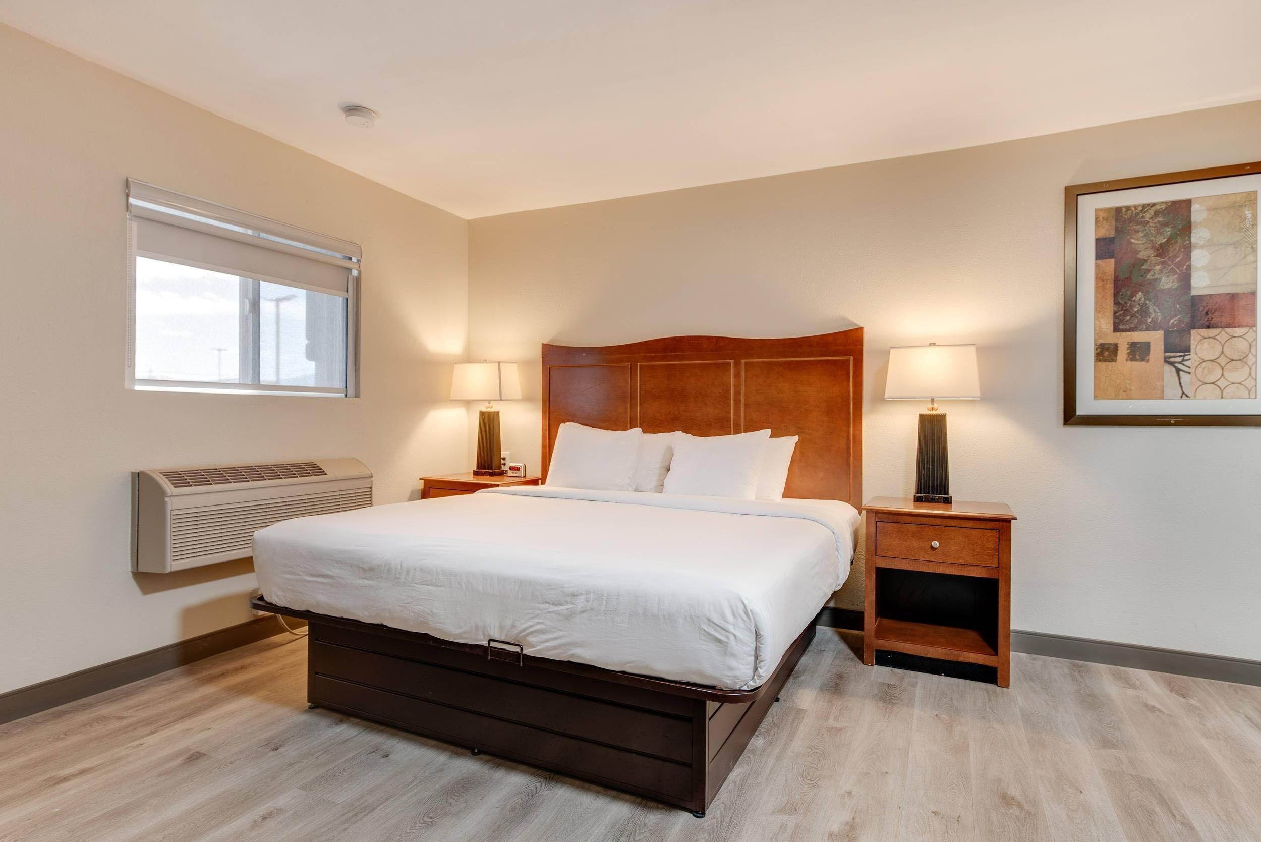 Une chambre d’hôtel avec un grand lit, deux tables de chevet avec des lampes, un climatiseur fixé au mur et une œuvre d’art encadrée accrochée au mur.