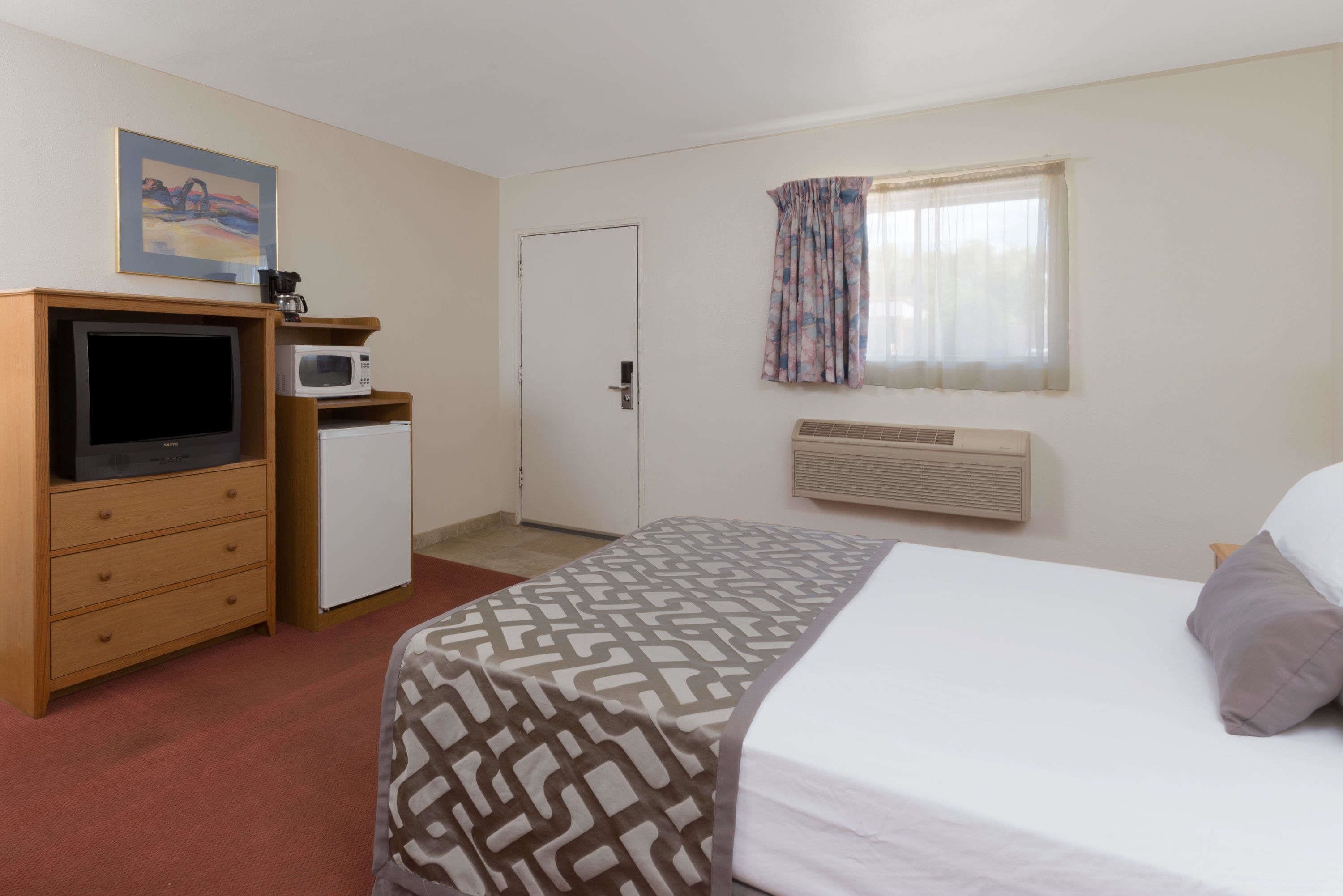 A hotel room with a bed, a desk with a computer, a microwave, and a small refrigerator.
