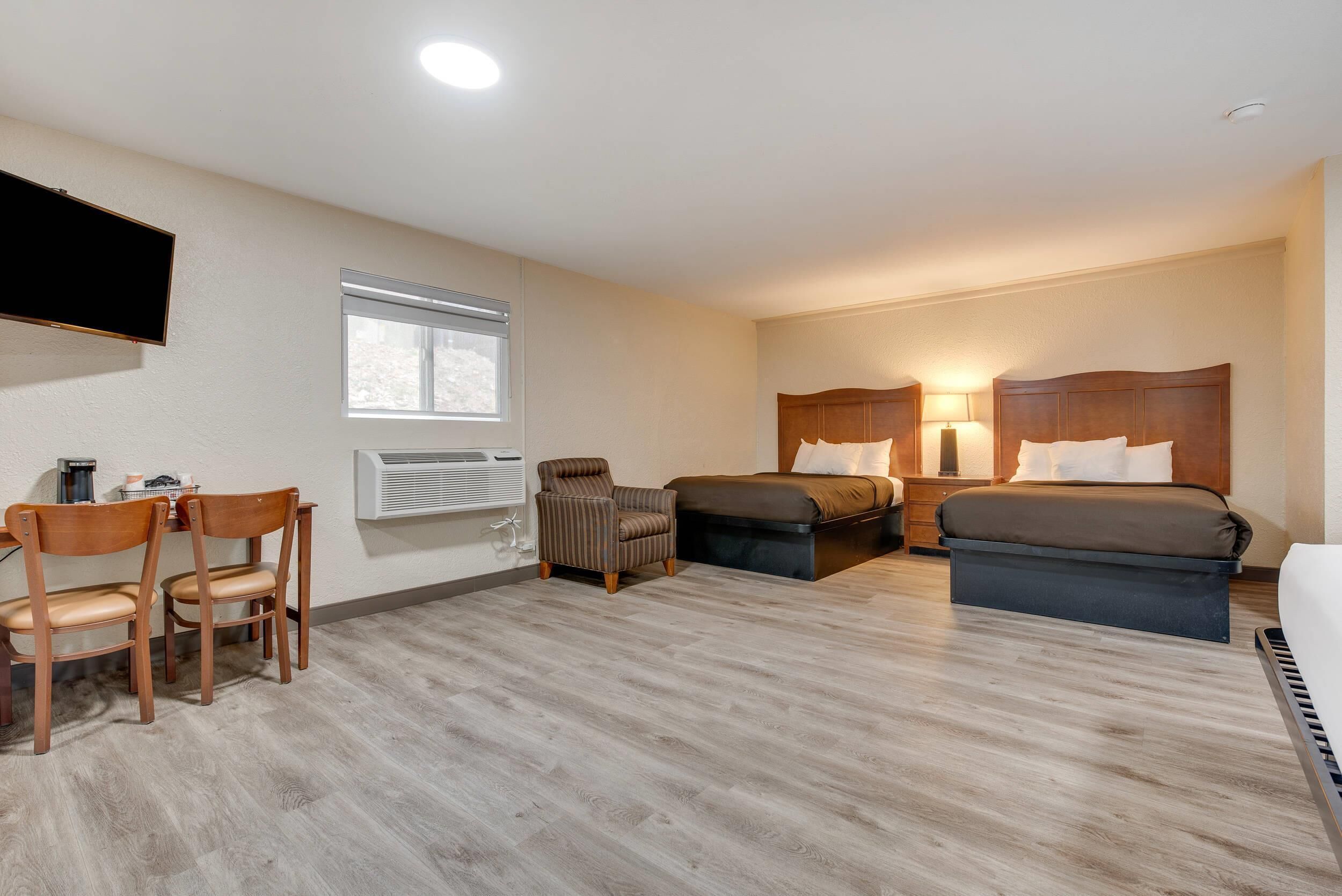 A hotel room with two beds, a desk, a chair, a TV, and a window.