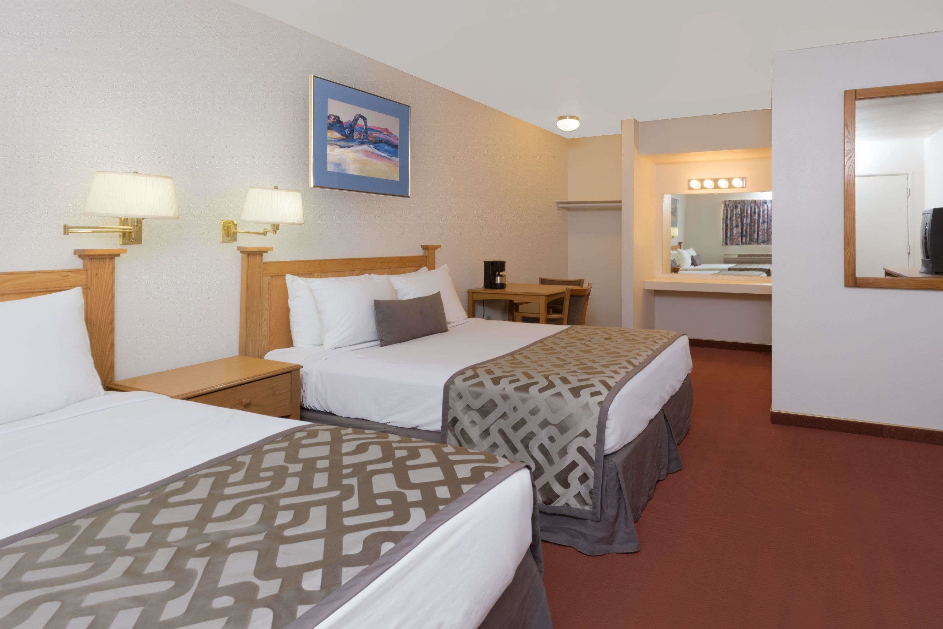 A hotel room with two beds, a desk, a mirror, and a painting on the wall.