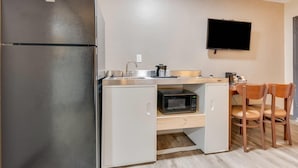 A compact kitchen with a refrigerator, microwave, sink, and a small cabinet. A flat-screen TV is mounted on the wall above the counter. - Suburban Studios near Mesa Verde (Cortez)