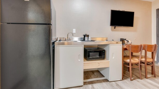 A compact kitchen with a refrigerator, microwave, sink, and a small cabinet. A flat-screen TV is mounted on the wall above the counter. - Suburban Studios near Mesa Verde (Cortez)