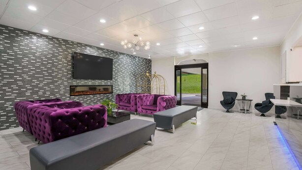 Un salon moderne doté d’une cheminée, de canapés violets, d’un téléviseur à écran plat et offrant une vue sur l’extérieur.