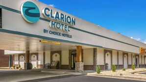 Un hôtel Clarion, membre du groupe Choice Hotels, doté d’une entrée couverte, de piliers en pierre et offrant une vue sur un ciel bleu dégagé.