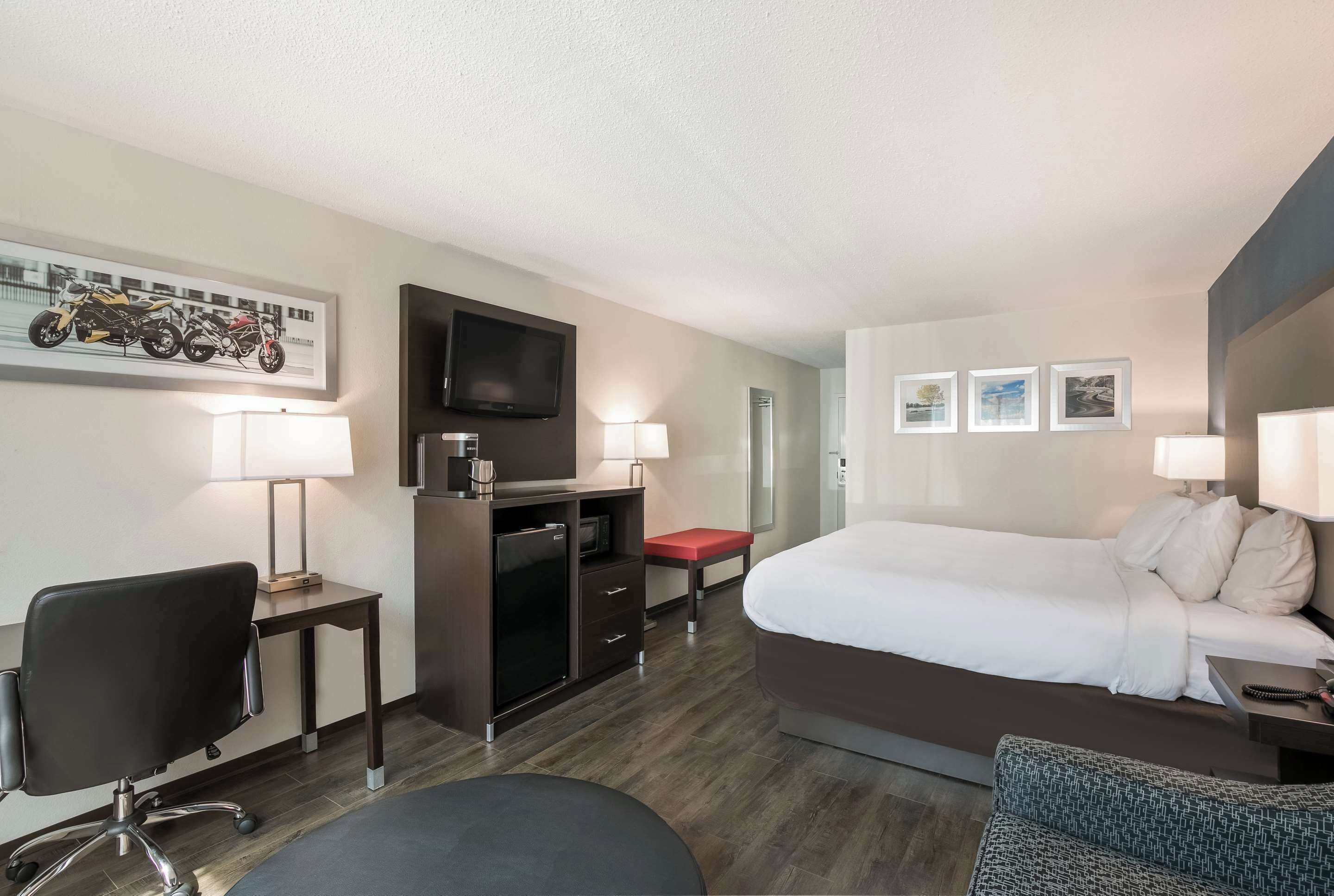 Ein Hotelzimmer mit Bett, Schreibtisch, Stuhl, Fernseher und einem kleinen Tisch.