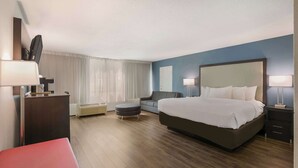 Une chambre d’hôtel avec un grand lit, un bureau, une chaise, un canapé et un petit pouf.