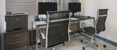 A modern office with two desks, each with a computer monitor, black mesh office chairs, and a Brother printer on a cabinet.