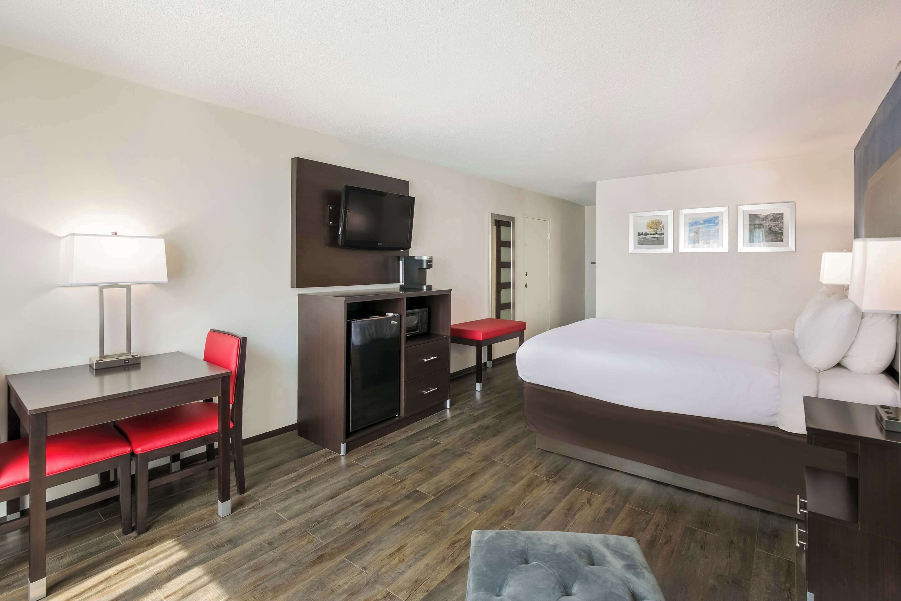 Habitación de hotel con cama, escritorio con silla, televisor y una pequeña cocina americana.