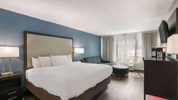 Habitación de hotel con una cama grande, mesitas de noche, un escritorio, una silla, un televisor y una ventana con cortinas.