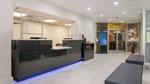 Un espace d’accueil moderne avec un comptoir sombre, un coin salon et, au fond, une enseigne de pizzeria.