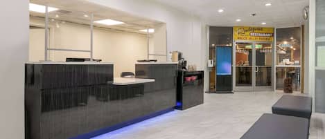 A modern reception area with a dark counter, a seating area, and a pizzeria sign in the background.