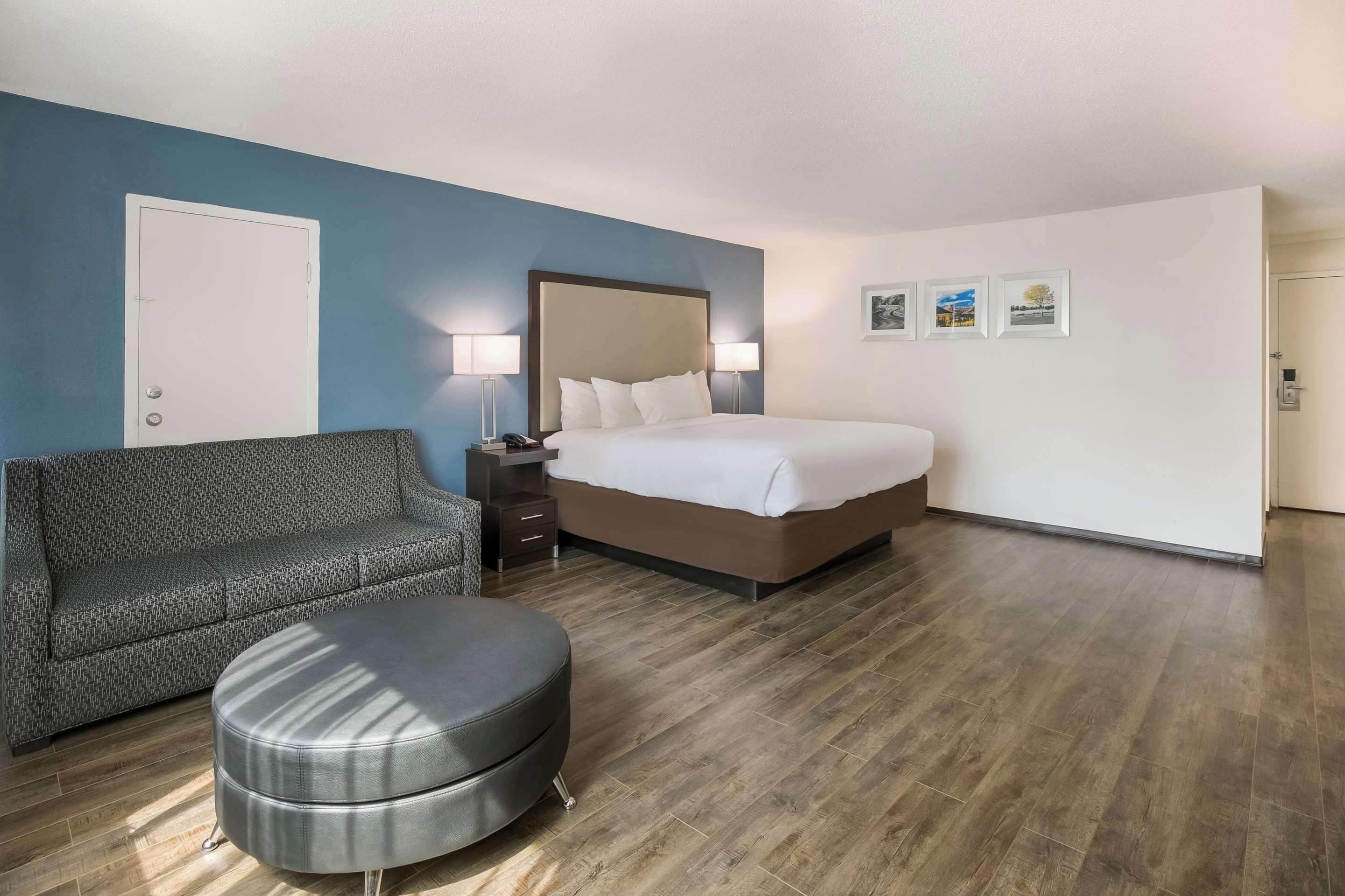 Une chambre d’hôtel comprenant un lit, un canapé, une table de chevet et un pouf rond.