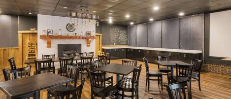 A restaurant with wooden tables and chairs, a brick wall, and a chalkboard menu.