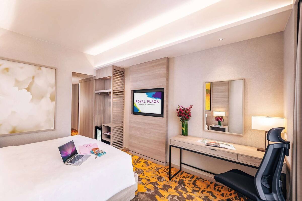 A hotel room with a bed, a desk, a chair, a TV, and a mirror.