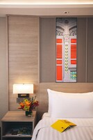 A hotel room with a bed, a nightstand with a lamp and a vase of flowers, and a wall-mounted artwork.