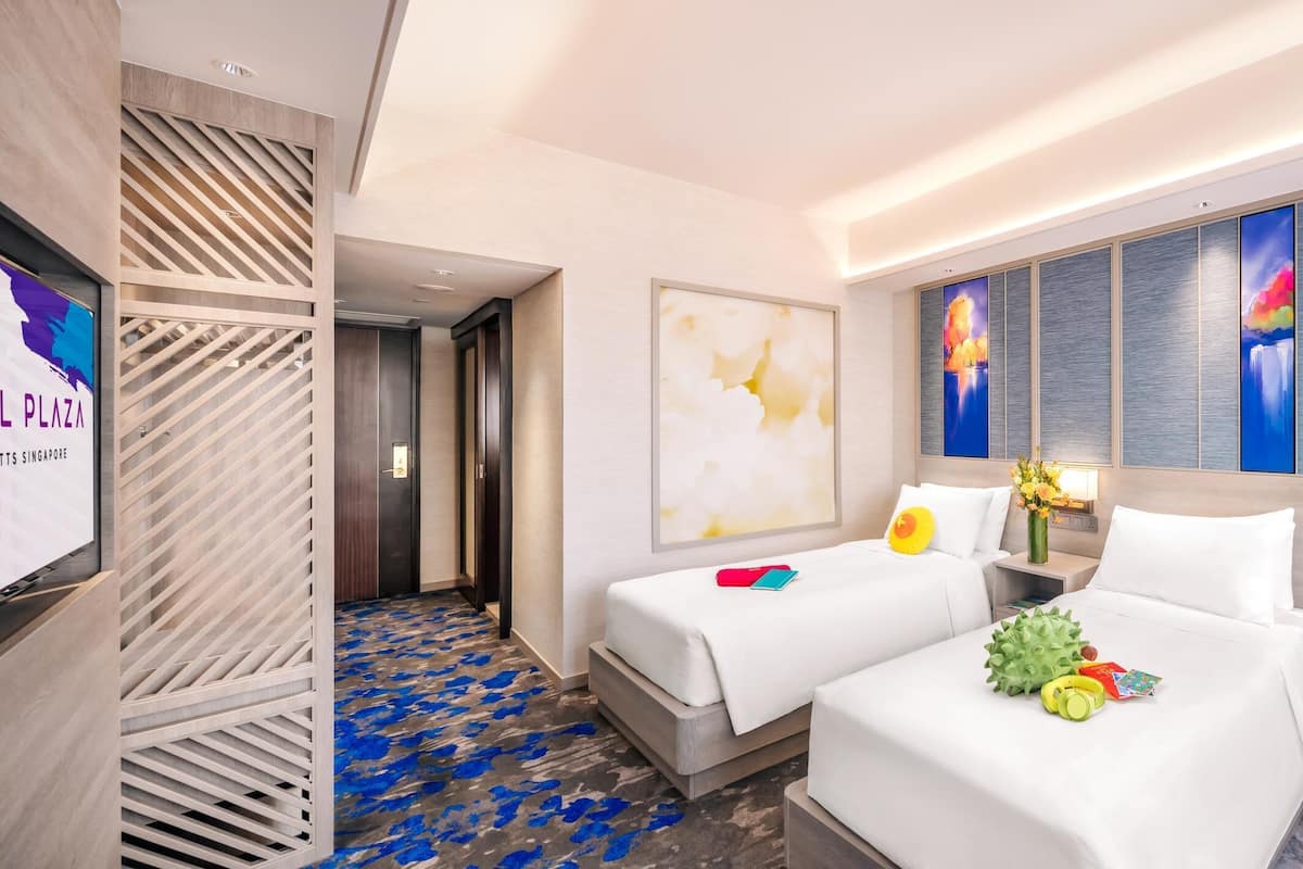 A hotel room with two beds, a blue armchair, and artwork on the walls.