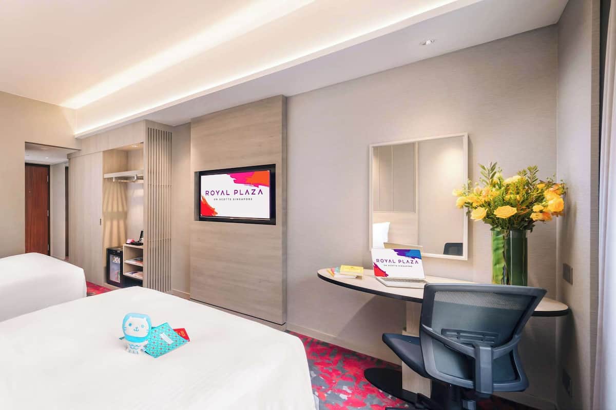 A hotel room with two beds, a desk, a chair, a TV, and a mirror.