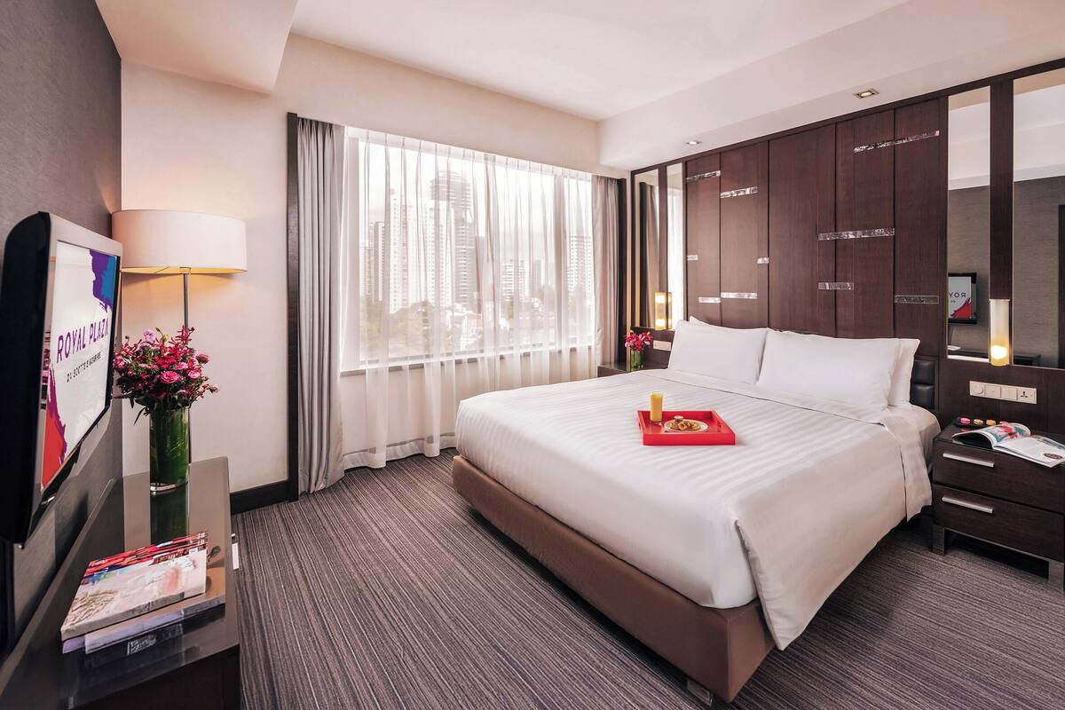A hotel room with a large bed, a nightstand with a lamp, a dresser, and a window with curtains.