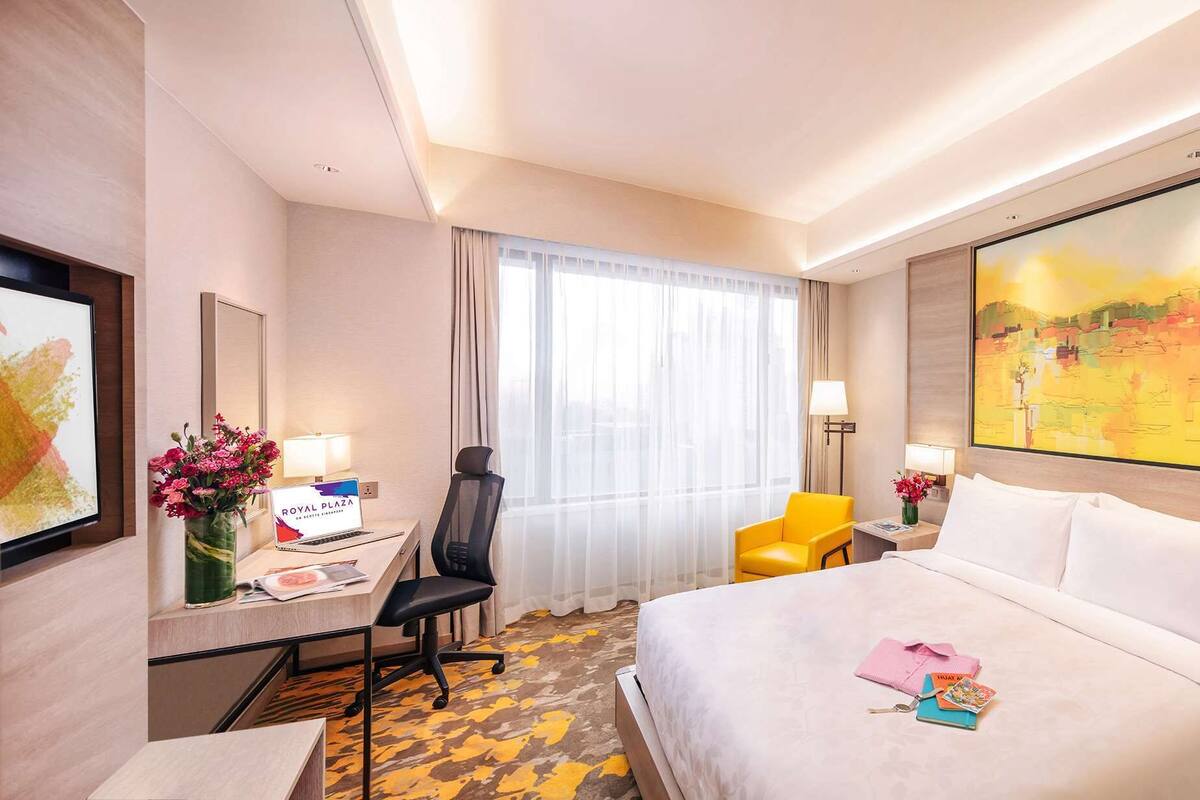 A hotel room with a bed, desk, chair, and a large painting on the wall.