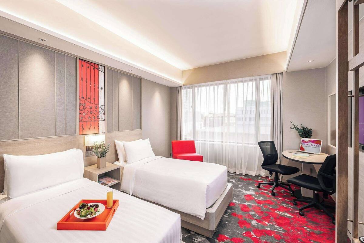 A hotel room with two beds, a desk, a chair, and a view of the city.