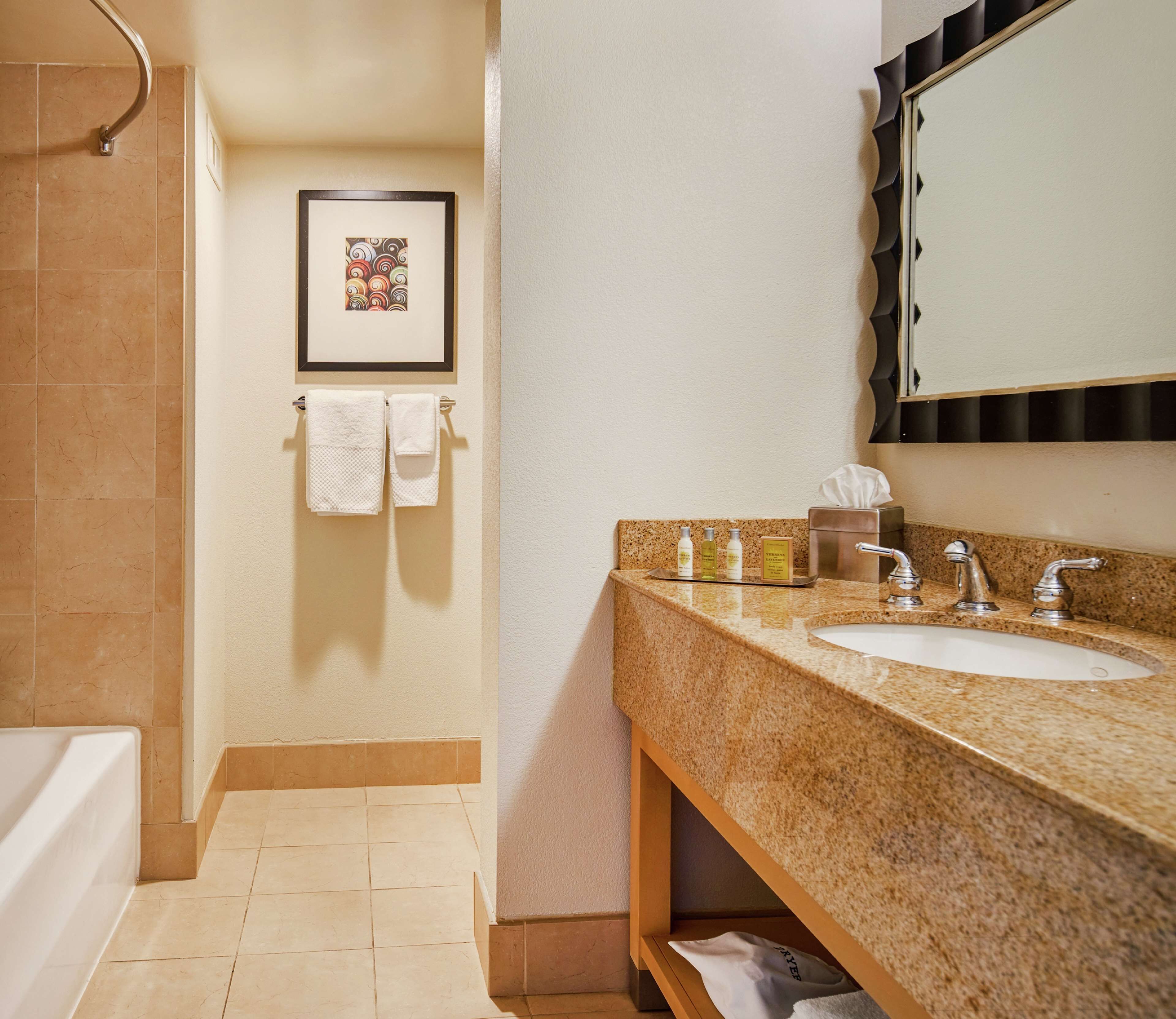 A bathroom with a sink, mirror, and shower. There are towels hanging on the wall and toiletries on the counter.