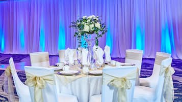 Ein festlich gedeckter Bankettisch mit weißen Tischdecken, goldenen Bändern und einer floralen Tischdekoration.