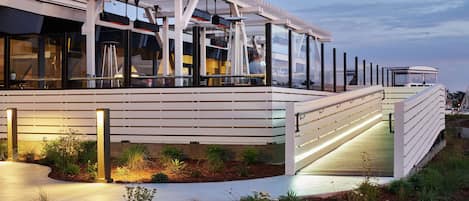 A modern outdoor seating area with a pergola, glass railings, and a pathway leading to a covered deck.