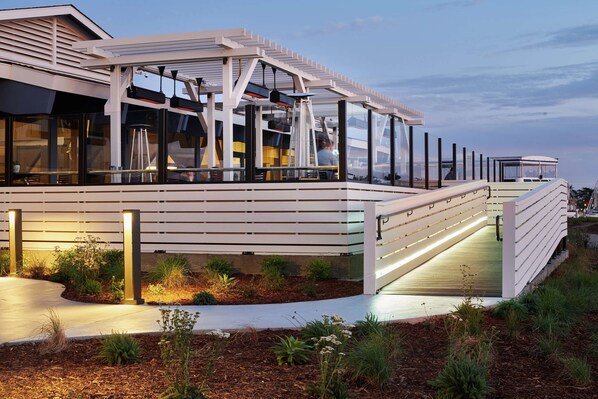 A modern outdoor seating area with a pergola, glass railings, and a pathway leading to a covered deck. - DoubleTree by Hilton Hotel Berkeley Marina (Berkeley)