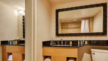 A bathroom with a black countertop sink, a wooden vanity, a mirror with a black frame, and a toilet.
