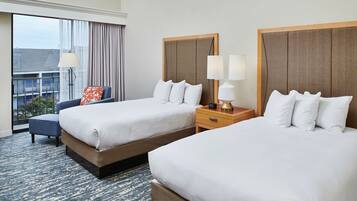 A hotel room with two beds, a chair, a nightstand, and a large window with curtains.