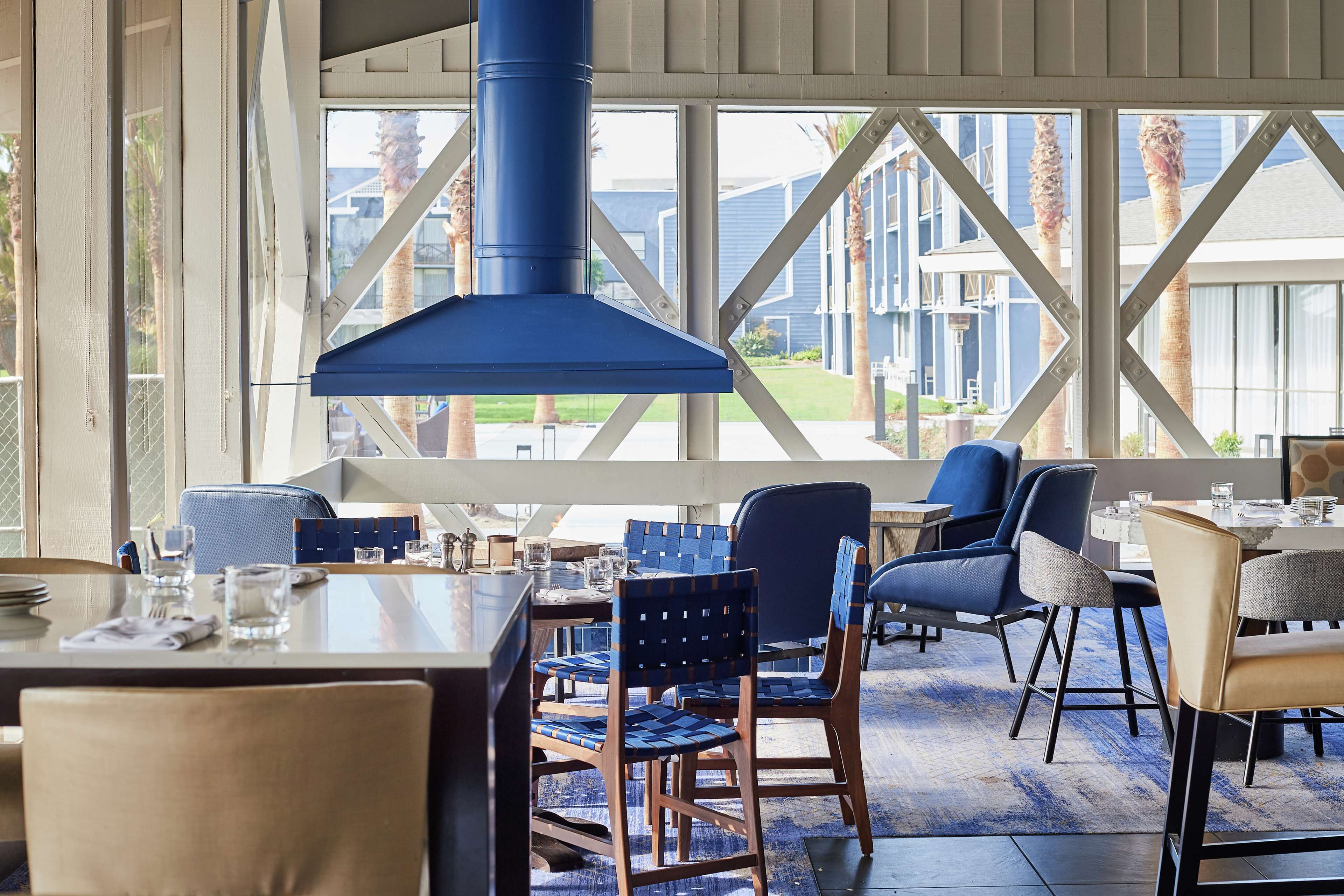 A dining area with a large window, blue chairs, and a blue ceiling vent.