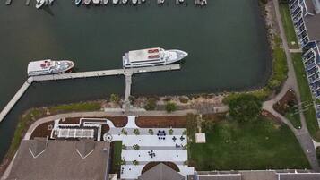 An aerial view of a marina with several boats docked, a pedestrian walkway, and a building with a distinct roofline.
