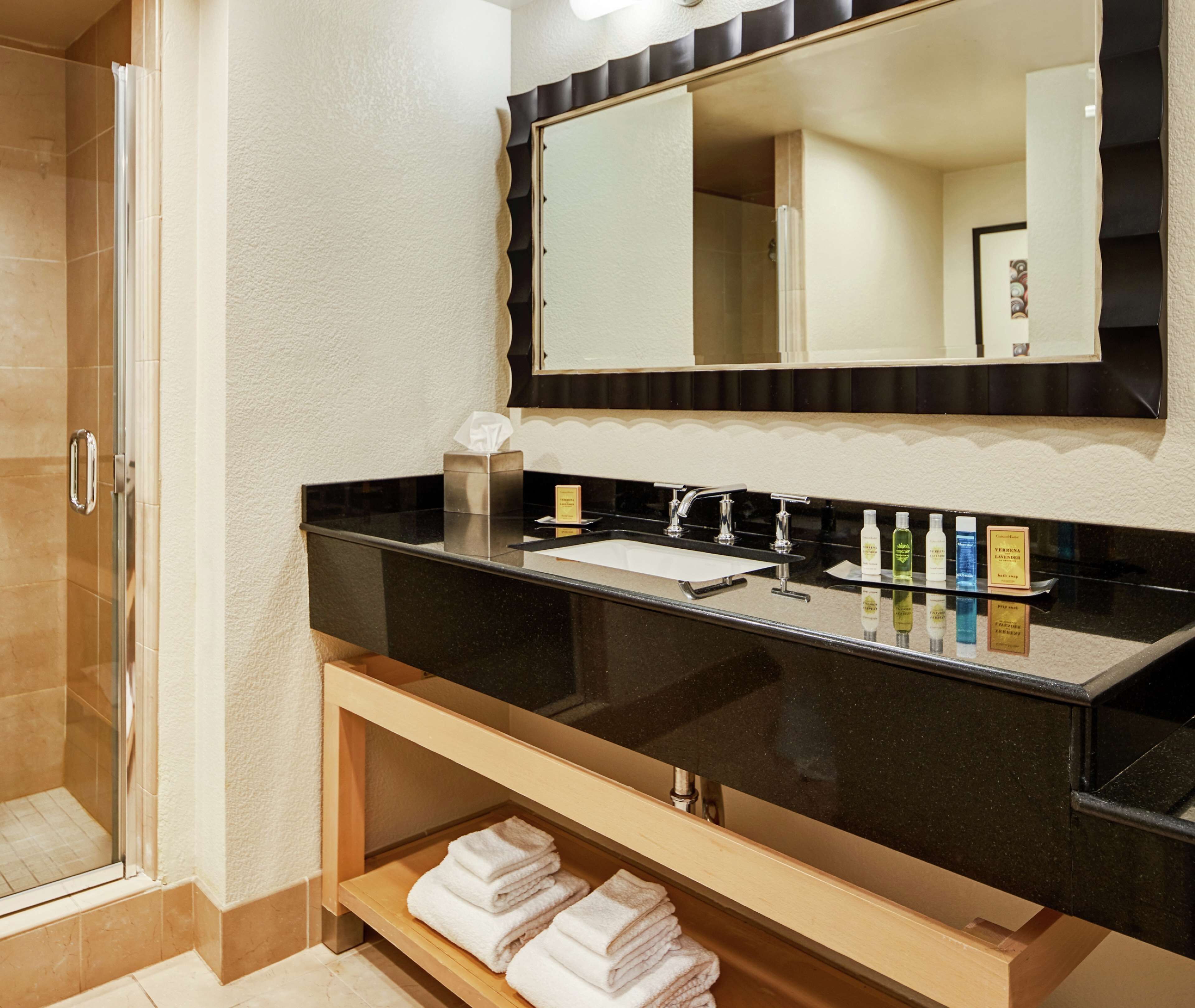 Un baño moderno con encimera negra, un espejo grande y cabina de ducha con mampara de vidrio.