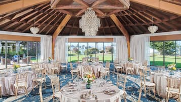 A banquet hall with round tables, chairs, and a chandelier.