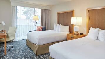 A hotel room with two beds, a desk, a chair, and a window with curtains.