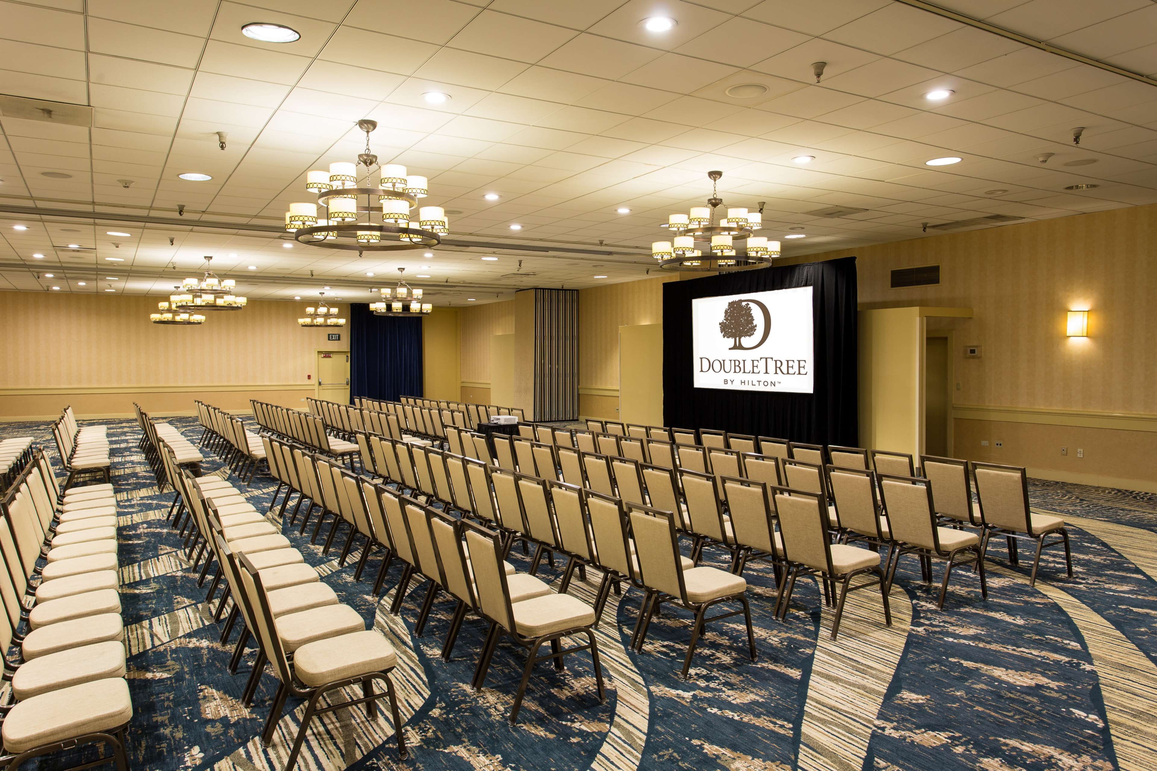 A conference room with rows of chairs, a stage with a screen, and chandeliers.