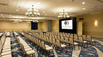 A conference room with rows of chairs, a stage with a screen, and chandeliers.