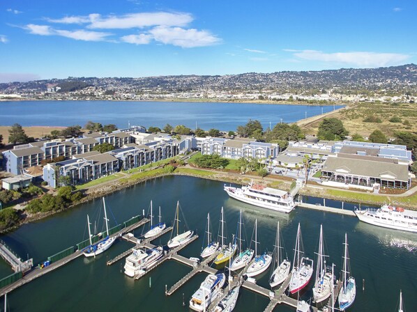 A marina with multiple boats docked, a large building with a flat roof, and a view of a distant cityscape.