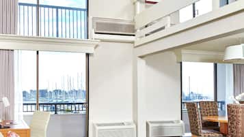 Habitación de hotel con balcón, ventanas amplias y zona de comedor con sillas y mesa.
