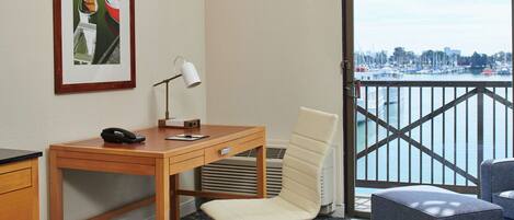 A hotel room with a bed, a desk with a telephone, a chair, a framed picture on the wall, and a view of a marina.
