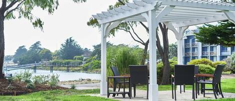 A gazebo with outdoor seating, overlooking a body of water and a bridge.