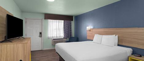 Una habitación de hotel con cama, escritorio, televisión y ventana con cortinas.