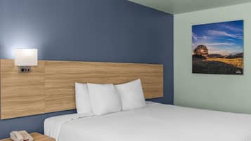 A hotel room with a wooden headboard, a bed with white bedding, a bedside lamp, a telephone, and a landscape painting on the wall.